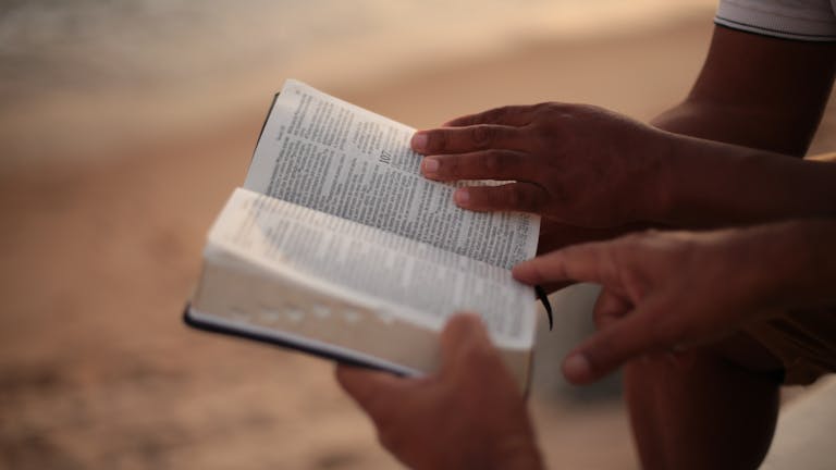 Close-up of hands holding an open Bible on a beach, symbolizing faith and study.